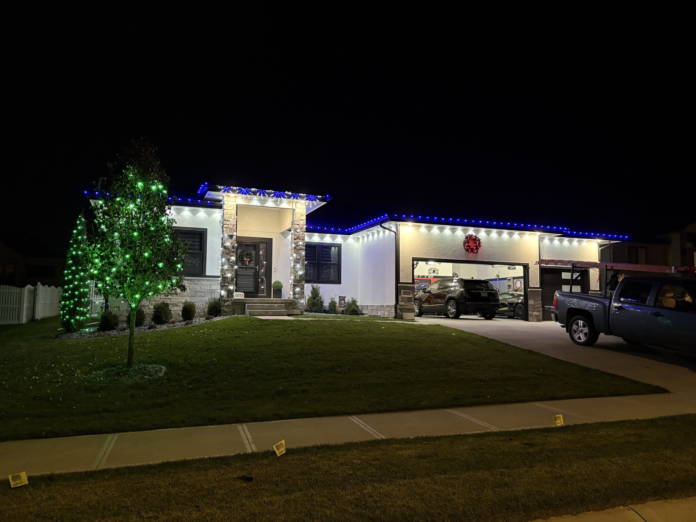 Ranch home with blue roofline lights and a front yard tree wrapped in green lights